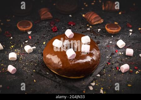 Chocolate glazed doughnut decotrated with marshmallows on black slate background, still life Stock Photo