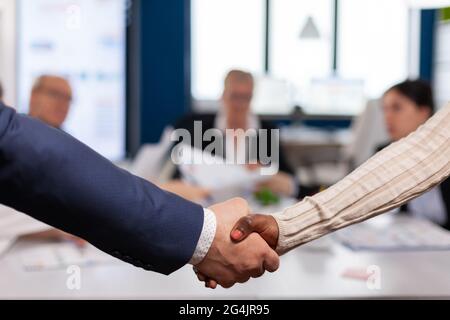 Close up of multiracial business partners standing in front of conference desk shaking hands after signing partnership contract. Diverse team being happy for successful negotiations in startup company Stock Photo