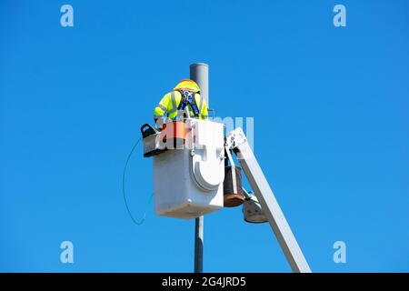 Technician works on installing or repairing a small cell antenna on a lamp post from the platform of the telescopic boom lift. Blue sky.