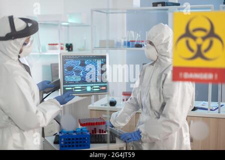Scientists in ppe suit talking behind the glass wall working in danger area of lab. Group of doctors examining vaccine evolution using high tech for diagnosis against covid19. Stock Photo