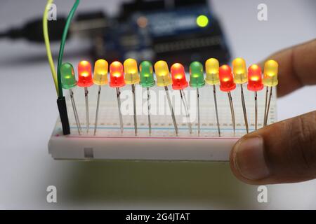 Light emitting diodes on breadboard with glowing lights controlled by micro controller board on background held in hand Stock Photo