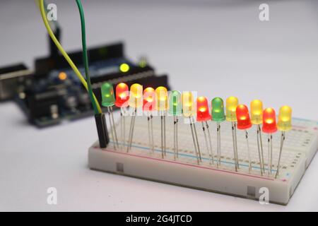 Glowing light emitting diode in short LED which is an Electronic component connected to breadboard with some micro controller on background Stock Photo