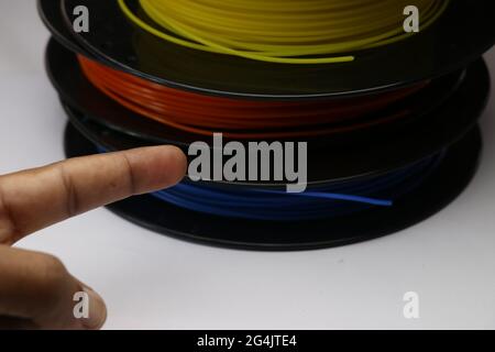 Hand pointing towards 3D printer filaments laid flat on spools with different colors. Concept showing to use thermoplastic which is biodegradable Stock Photo