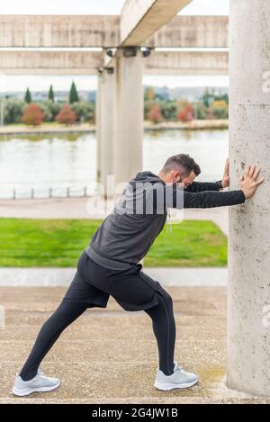 Runner with mask stretching in a park leaning against a wall. Stock Photo