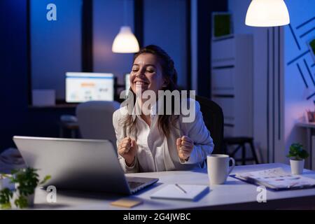 Happy businesswoman reading great online news on laptop working on economic opportunity at start up company office. Employee using modern technology network wireless studying financial statistics Stock Photo