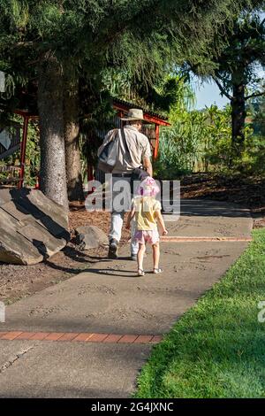 Mackay, Queensland, Australia - June 2021: A grandfather carrying bags walks with his little granddaughter in the botanic gardens showing her the plan Stock Photo