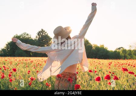 Young woman dancing on poppy field from back