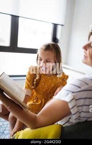 Portrait of pregnant mother and daughter reading a book in living-room Stock Photo