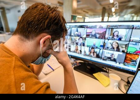 Coronavirus outbreak, Covid 19, remote working, video conference in a company. Man sitting at his desk holding his head with his hands Stock Photo