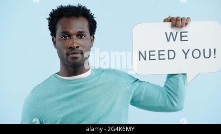 african american employer holding speech bubble with we need you lettering isolated on blue Stock Photo