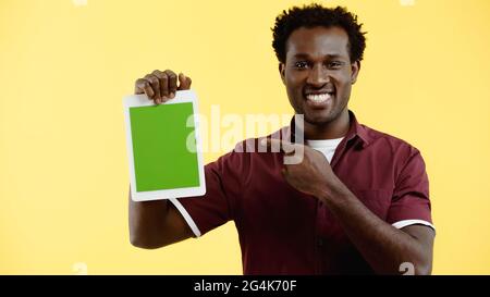 cheerful african american man in burgundy shirt pointing at digital tablet with green screen isolated on yellow Stock Photo