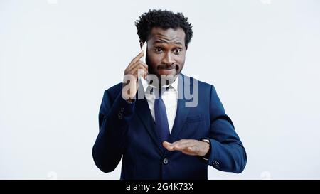 dissatisfied african american businessman talking on smartphone isolated on blue Stock Photo