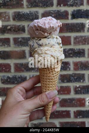 woman's hand holding a waffle cone with three scoops of ice cream Stock Photo