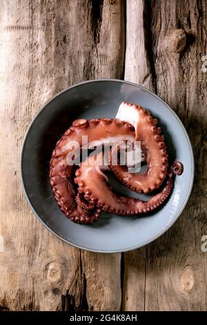 Coocked tentacles of octopus on blue ceramic plate over brown wooden background. Top view, flat lay Stock Photo
