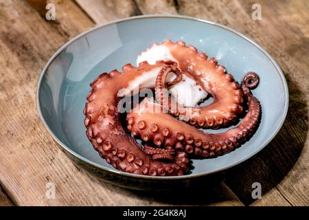 Coocked tentacles of octopus on blue ceramic plate over brown wooden background Stock Photo