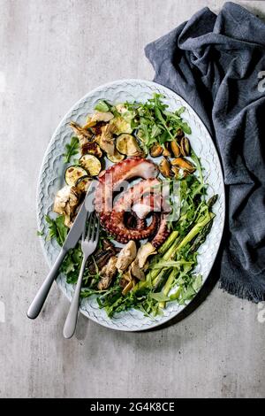 Seafood salad. Coocked grilled tentacles of octopus, sardines and mussels on blue ceramic plate served with arugula salad, zucchini and asparagus over Stock Photo
