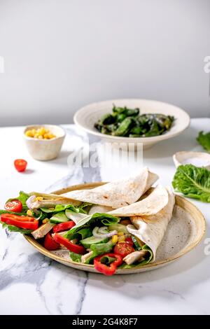 Traditional mexican tortila wrap with pork meat and vegetables in ceramic plate served with grilled green peppers jalapenos and corn over white marble Stock Photo