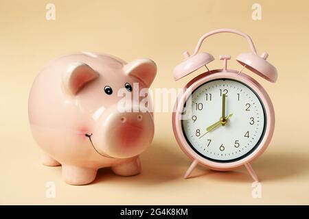 Piggy bank and pink alarm clock on beige background Stock Photo