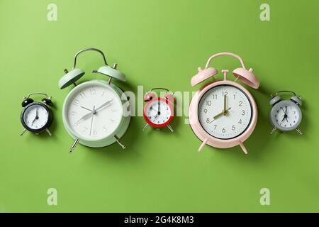 Different multicolor alarm clocks on green background Stock Photo