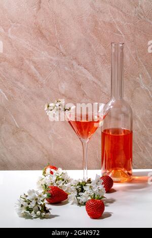 Concept of strawberry alcoholic or non-alcohol cocktail in martini glass, and glass bottle decorated with blooming branches of cherry tree over white Stock Photo