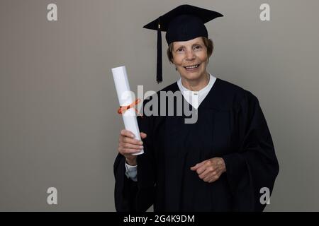 smiling older woman graduate in graduation gown holding diploma Stock Photo