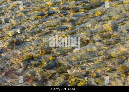 Sea stones in clear sea water. Textured abstract background in neutral beige shades. Beautiful ripples on the water shimmer in the sunlight. Natural s Stock Photo