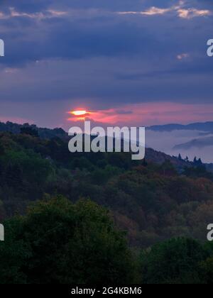 The rising sun peeks from behind heavy rain clouds with a dense fog in the valley. Stock Photo
