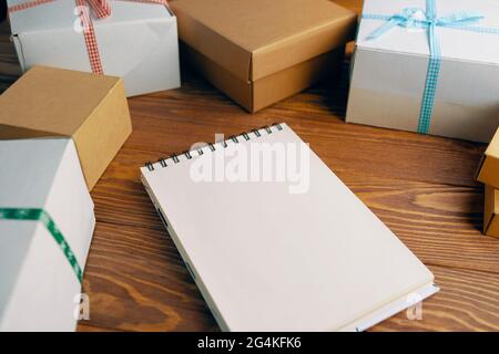Wooden table with gift boxes and blank spiral bound notepad. Space for writing wishes. Boxes are tied with colored ribbons. Concept of Christmas new year or birthday. Stock Photo