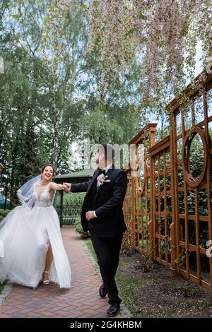 Cheerful groom holding hand of bride while walking in park Stock Photo
