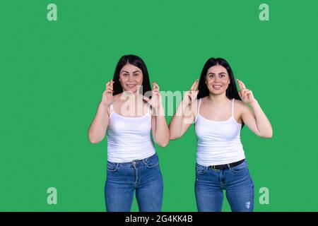 Tweens girls. Green background. They are wearing blue jeans and white shirt. Hair black and long. Girl are smiling. Stock Photo