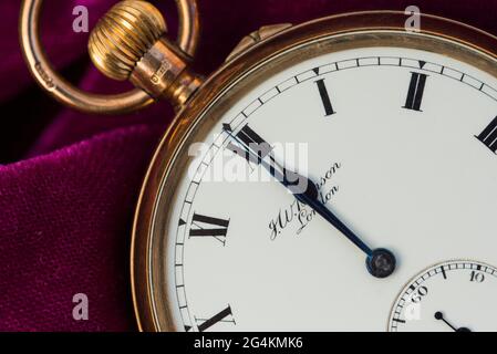 Seconds to midnight. Close up of a pocket watch on magenta velvet. Stock Photo