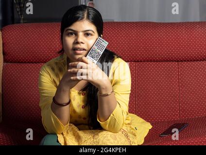 An Indian housewife woman watching television immersively holding remote in hand Stock Photo