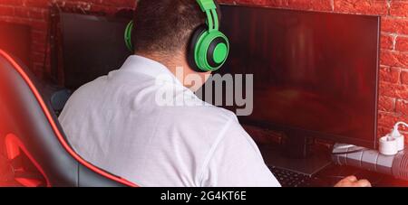 Guy in green headphones playing video games on the computer. Stock Photo