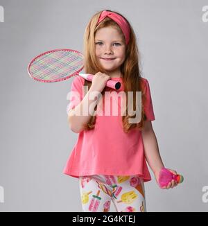 Happy smiling kid girl in pink clothes holds a badminton racquet on her shoulder and shuttlecock in hand Stock Photo