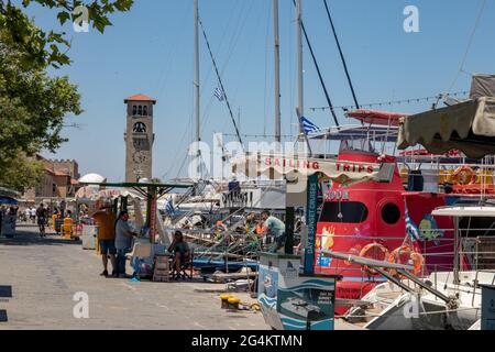 RHODES, Greece – JUN 07, 2021. Mandraki Harbour in Rhodes with the bell tower of the Church of the Evangelismos (Annunciation) with deer statue. Stock Photo