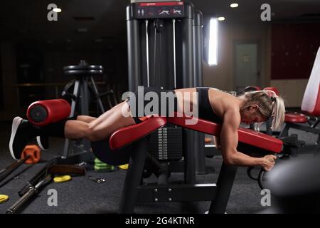 Fitness woman doing leg curls at the press machine in the gym Stock Photo