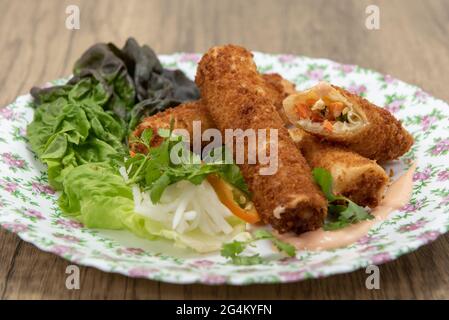 Hearty appetizer of breaded, deep fried egg rolls full of vermicelli and vegetables served on a flowered plate. Stock Photo