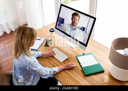 Businesswoman sitting at desk behind her computer and having online meeting while working from home. Home office. Stock Photo