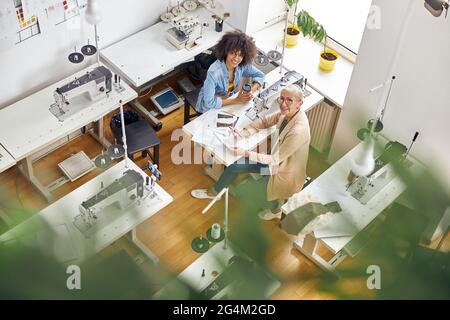 Mature fashion designer and African-American assistant with dresses drawings in studio view from above Stock Photo