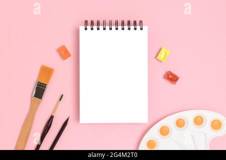 Empty notepad mockup and tools for painting on a pink background. Artistic workspace with copyspace. Stock Photo