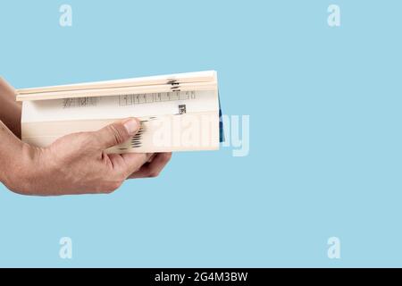 Close-up of man's hand holding and opening a thick book isolated on blue pastel color background. Stock Photo