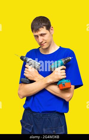 Young guy with screwdrivers in his hands on a yellow background. A worker in a blue T-shirt holds a tool and smiles. Layout Stock Photo
