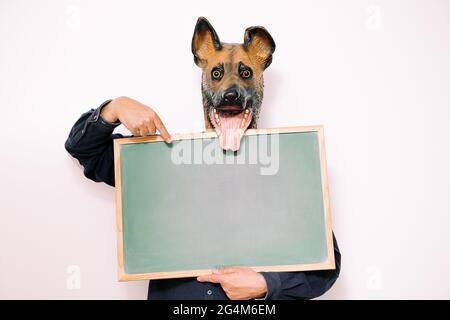 person with happy dog mask points to a blank sign on white background, copy space for text Stock Photo