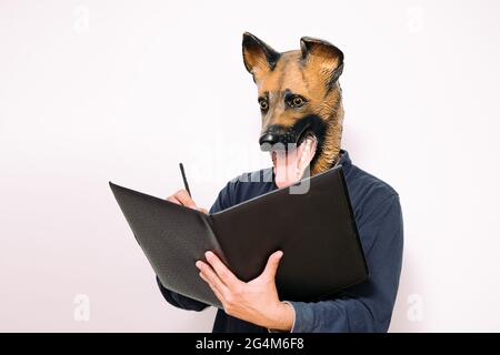 person with a dog mask taking notes in a notebook on white background, concept of a reliable veterinary clinic for your pet Stock Photo