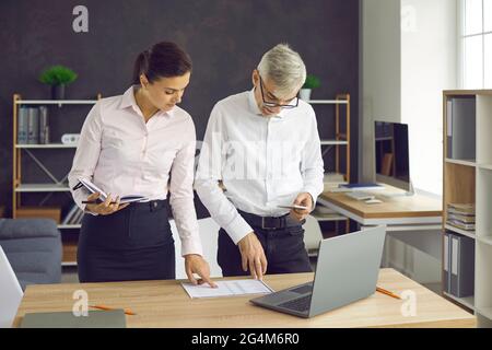 Two business colleagues standing by the office desk and working with some documents Stock Photo