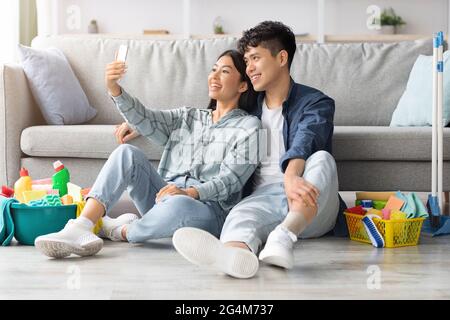 Loving chinese couple with cleaning tools taking selfie, using smartphone Stock Photo
