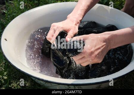 Young girl washes clothes by hand in basin. Hand wash clothes in nature. Washing clothes in the lake. Stock Photo