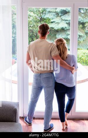 Rear view shot of couple standing together inside while looking out the window. Stock Photo