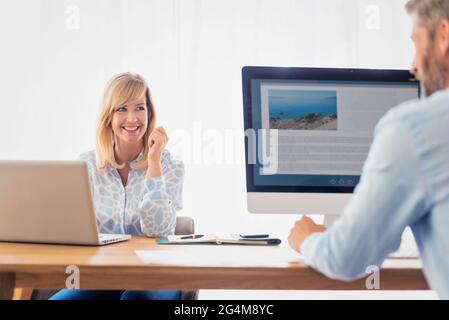 Shot of happy business woman working on laptop while her colleague sitting opposite to her and discussing about business. Teamwork. Stock Photo