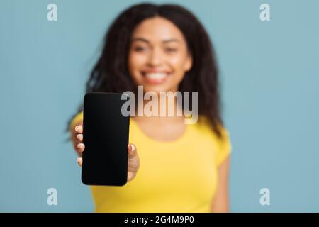 Mobile app concept. Happy african american woman showing smartphone with blank screen over blue background Stock Photo